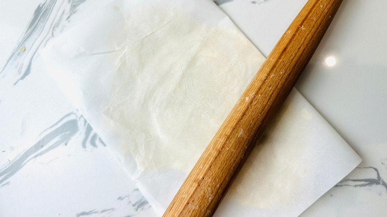 Dough pressed in between parchment paper with rolling pin on top