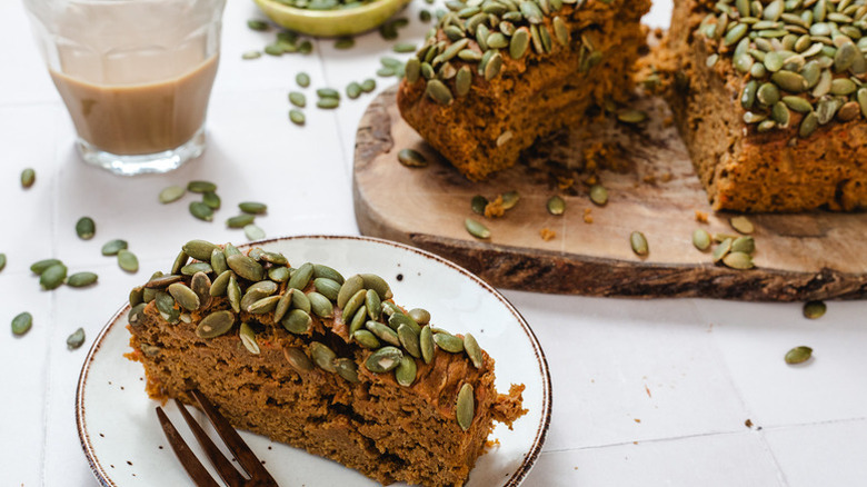 Pumpkin bread on wooden serving board next to slice on plate