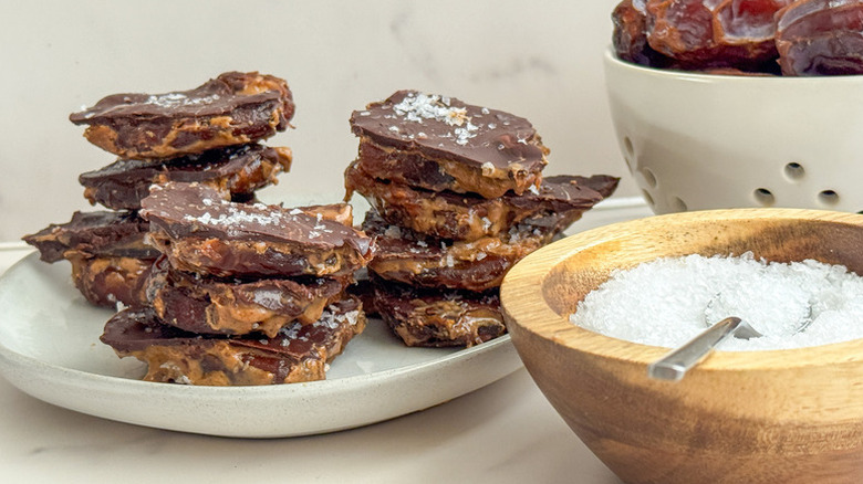 Chocolate date bark stacked on plate next to bowl of flaky sea salt