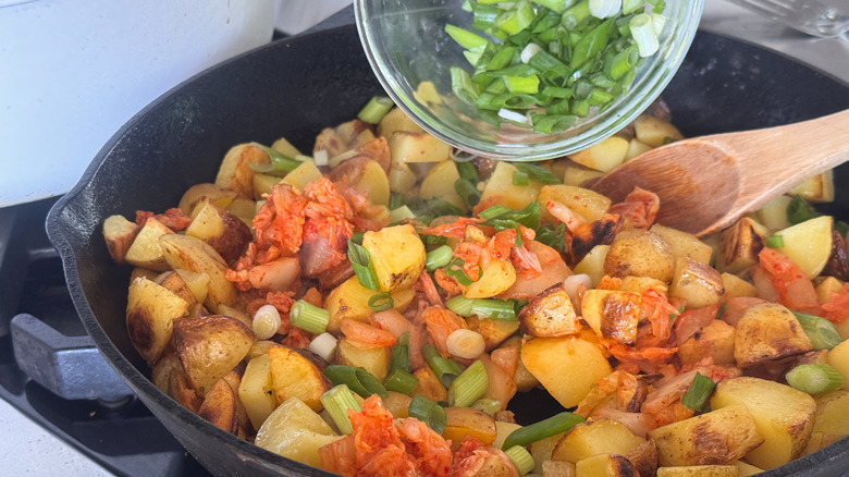 adding scallions to pan with potatoes