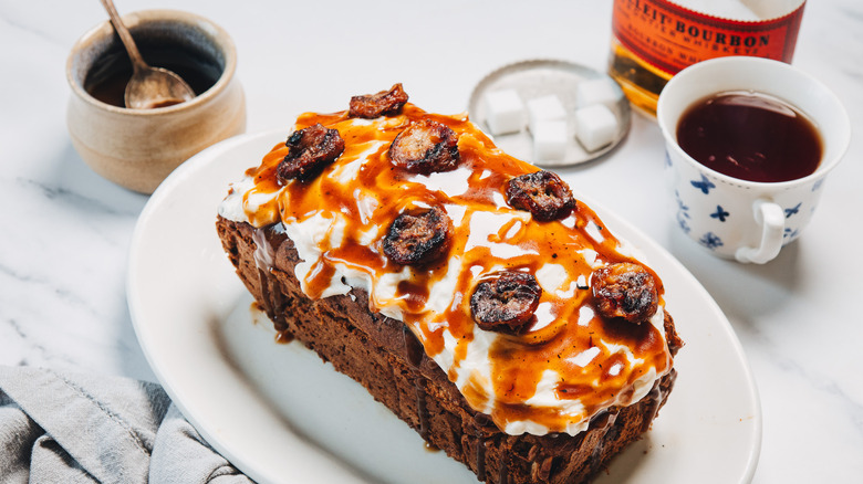 Bourbon banana bread on platter with banana slices, bourbon sauce, tea, and a bourbon bottle.