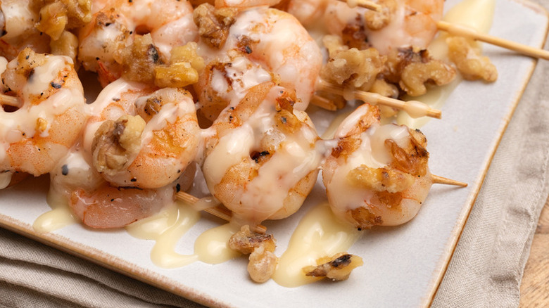 Skewered walnut grilled shrimp on plate, drizzled with creamy sauce