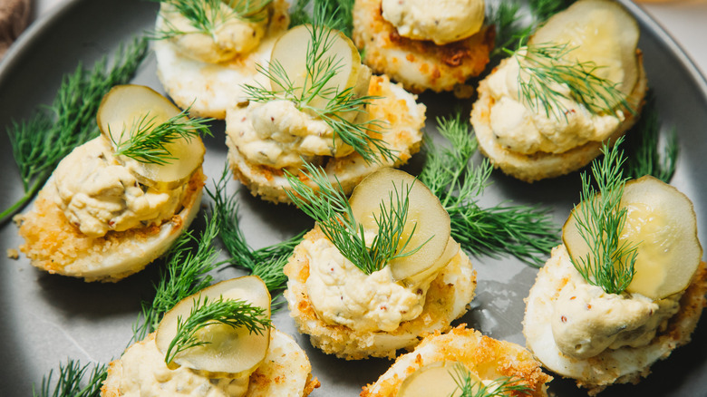 Close up on pickle and dill topped deviled eggs on a grey plate.