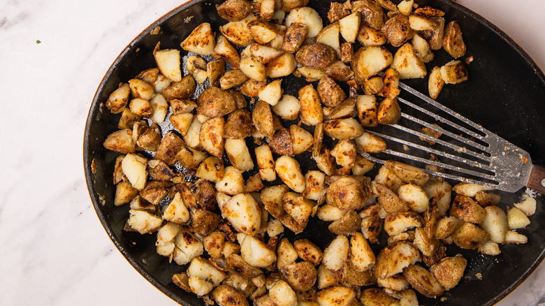 cast iron pan with seared potatoes and spatula