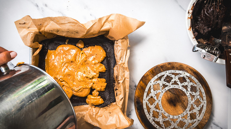Pouring caramel onto brownie layer.