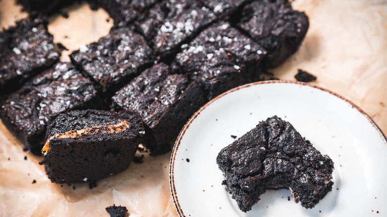 Gooey caramel-filled brownies with one on a plate with a bite taken out.
