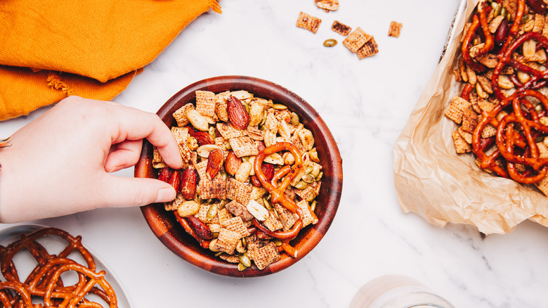 Hand picking up an almond from the spicy savory snack mix.