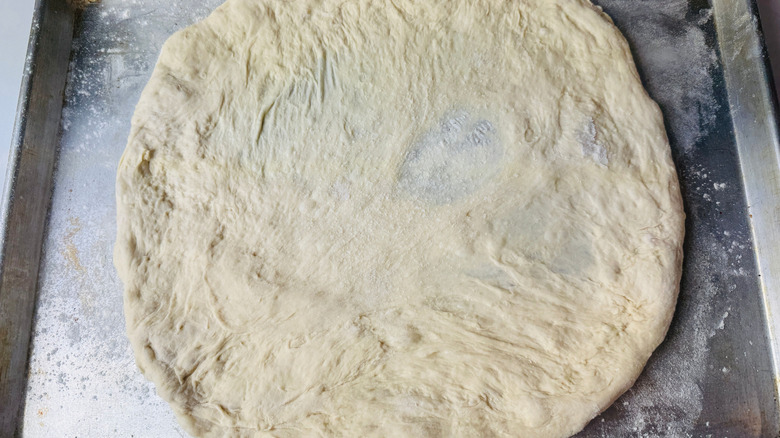 Stretched out pizza dough round on baking sheet