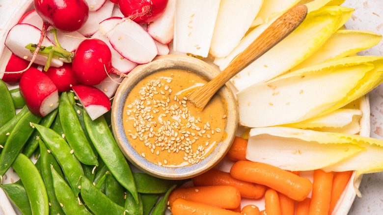 Overhead view of sesame dressing in small bowl with vegetables all around.