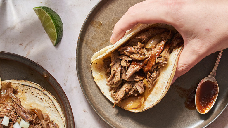 Hand placing a beef barbacoa taco on a plate