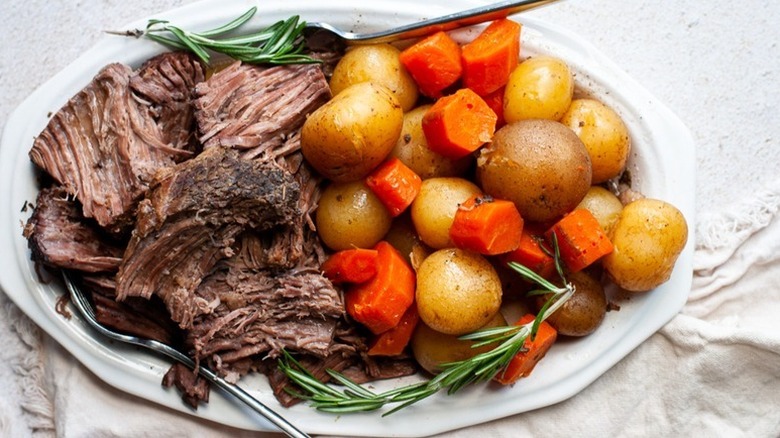 Slow-cooked beef on a serving plate with boiled potatoes and carrots