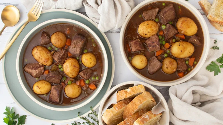 Two bowls of slow-cooked beef stew with potatoes, carrots, and peas