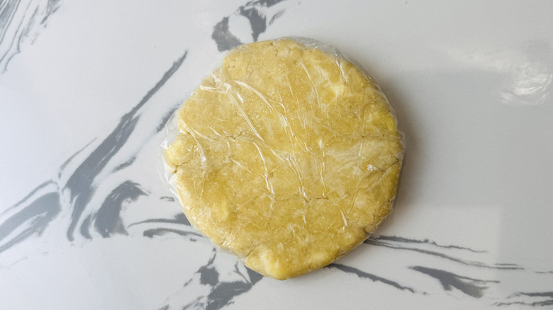 A disk of pie dough wrapped with plastic