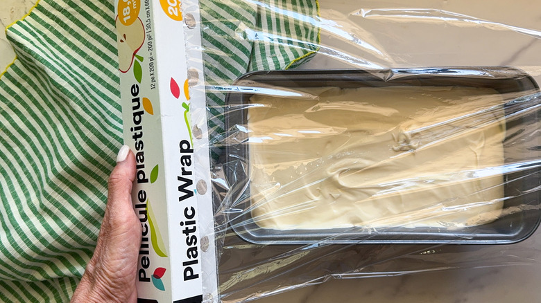 hands covering loaf pan with plastic wrap