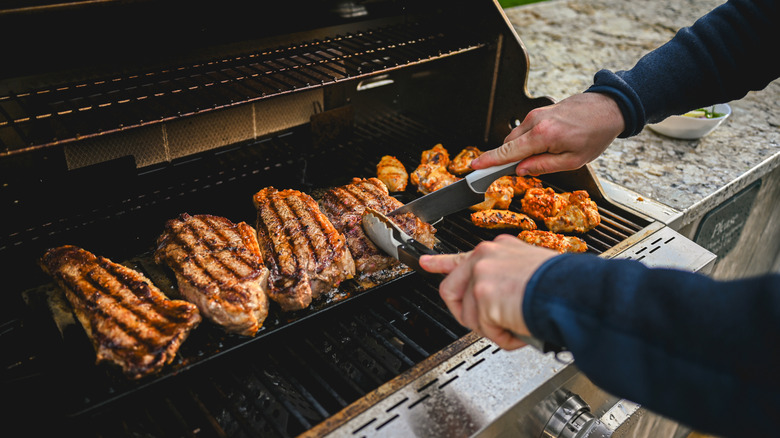 Person's hands as they turn meats on a gas grill