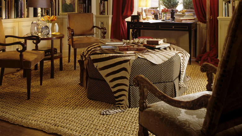 A zebra print throw is draped over a large round ottoman in the living room of a modern home.