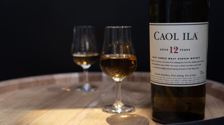 A bottle of Caol Ila 12-year placed on top of a barrel next to a couple of filled glasses