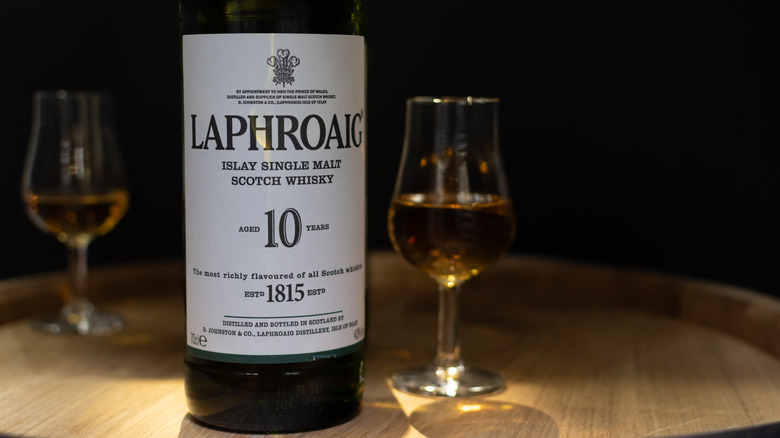 A bottle of Laphroaig 10-year placed on top of a barrel next to two filled glasses