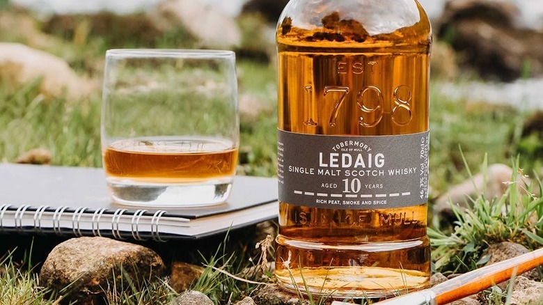 A bottle of Ledaig 10-year placed outside next to a filled glass on top of a notebook