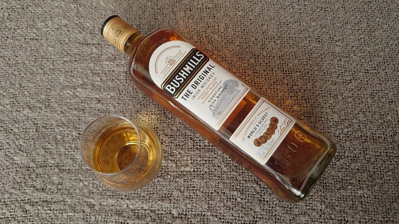 A top down shot of a bottle of Bushmills Original laid diagonally next to a filled glass