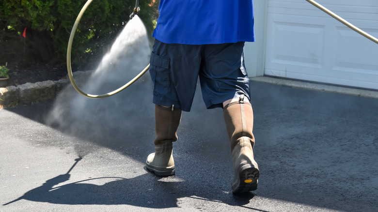 A person spraying water on an asphalt driveway