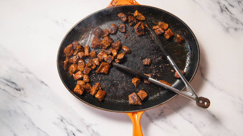 Seared steak bites in pan with tongs