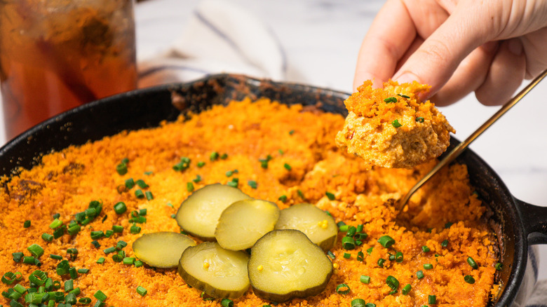 Hand holding a dipped cracker over Nashville hot chicken dip