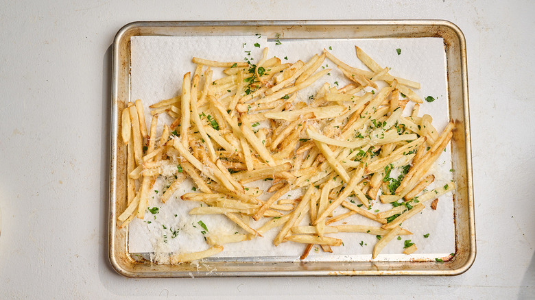 french fries tossed with parsley and parmesan on a sheet tray