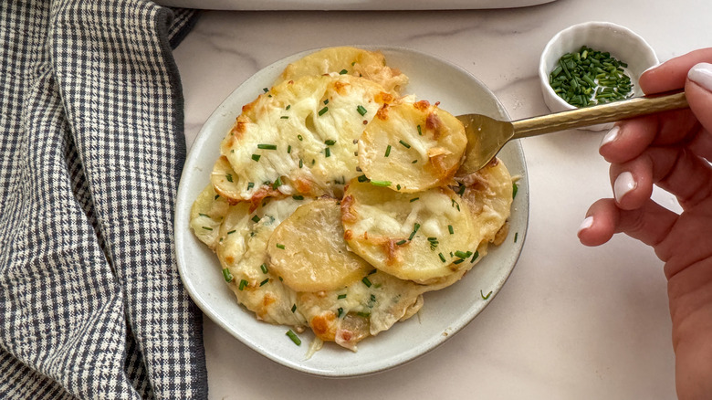 hand using fork to grab bite of cheesy potatoes off plate