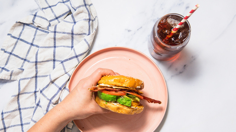 Hand holding breakfast burger over plate