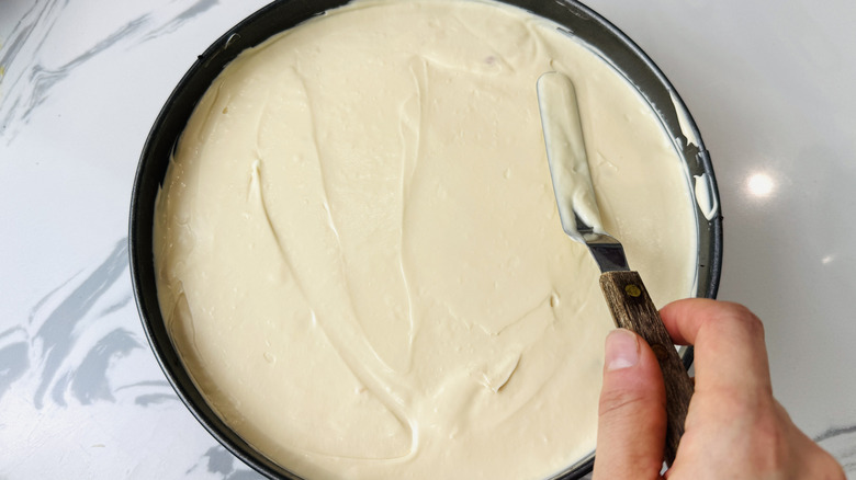 Hand smoothing out cheesecake filling in pan with offset spatula