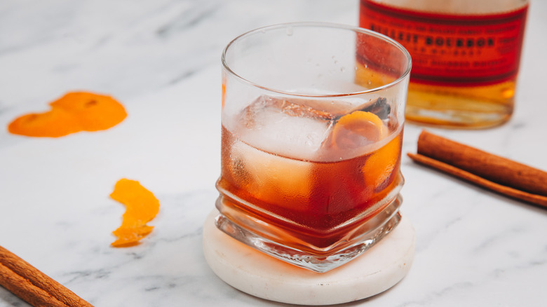A glass of a brown butter old fashioned with bourbon in background