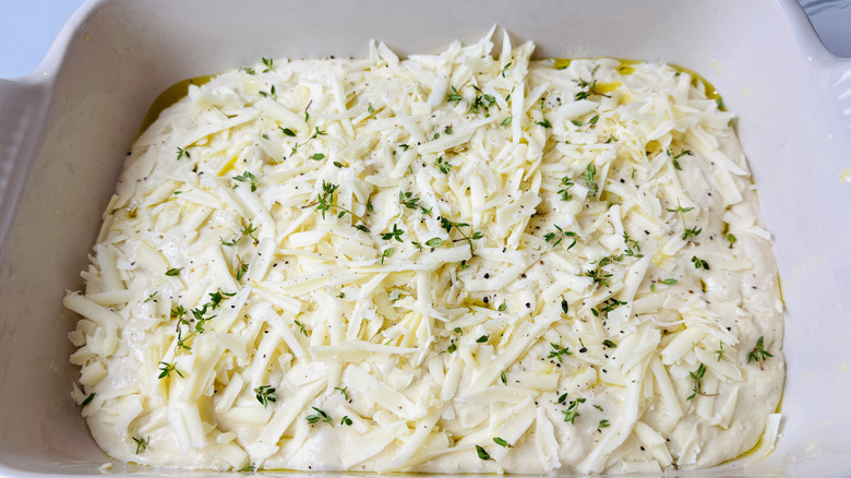 Focaccia dough topped with shredded cheese and thyme