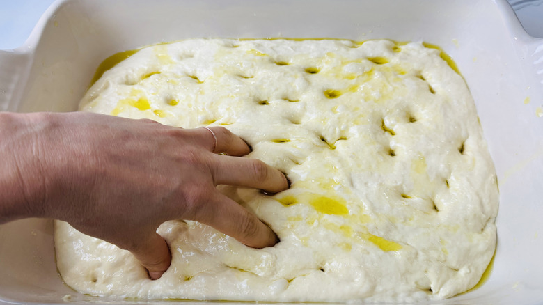 Hand pressing fingertips into focaccia dough