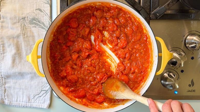 Stirring tomato paste into tomatoes and shallots cooking in Dutch oven on stovetop