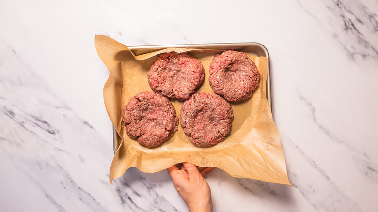Uncooked burger patties on baking sheet