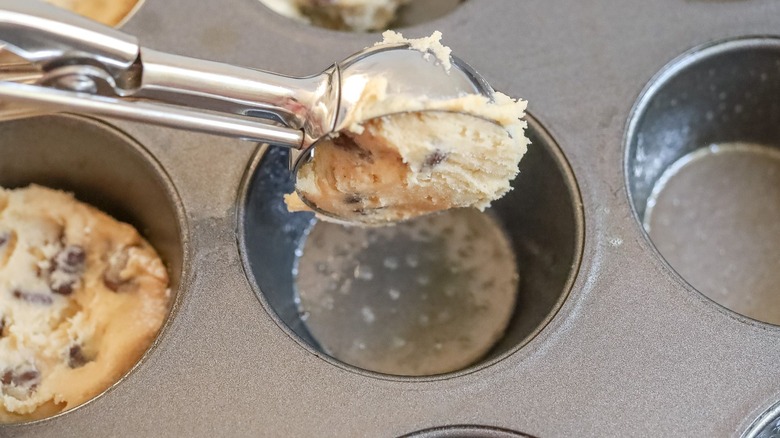 Scoop of cookie dough going into muffin pan well