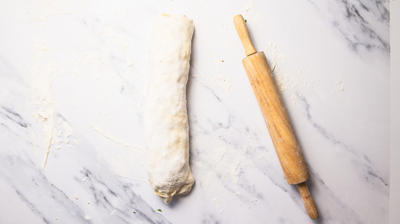 Stuffed puff pastry rolled into log next to rolling pin